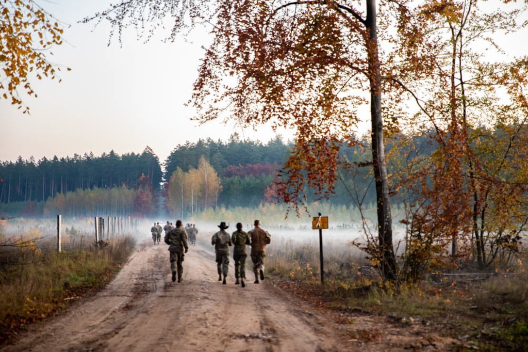 Soldiers run along a dirt road.