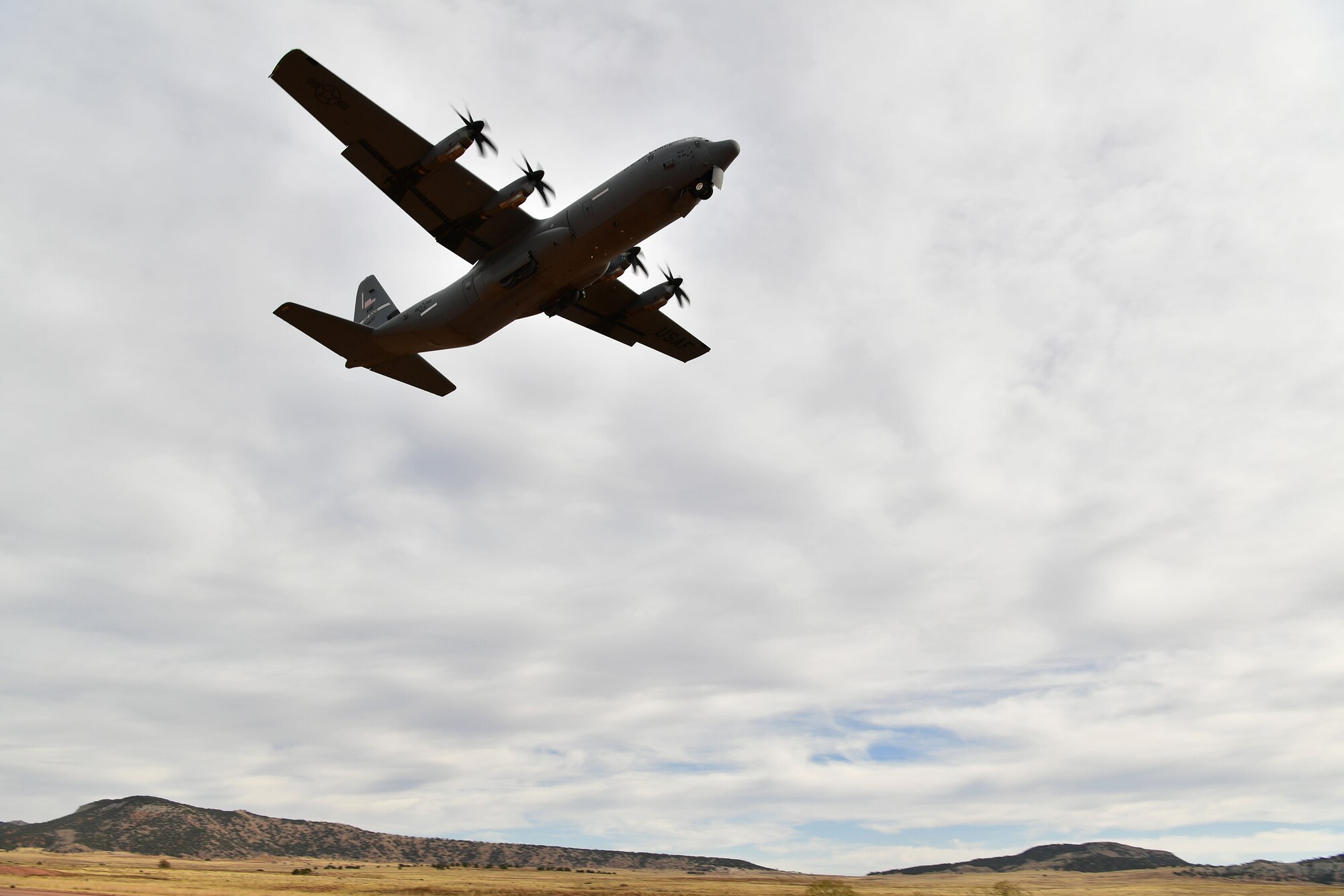 A C-130 takes off from a dirt runway.