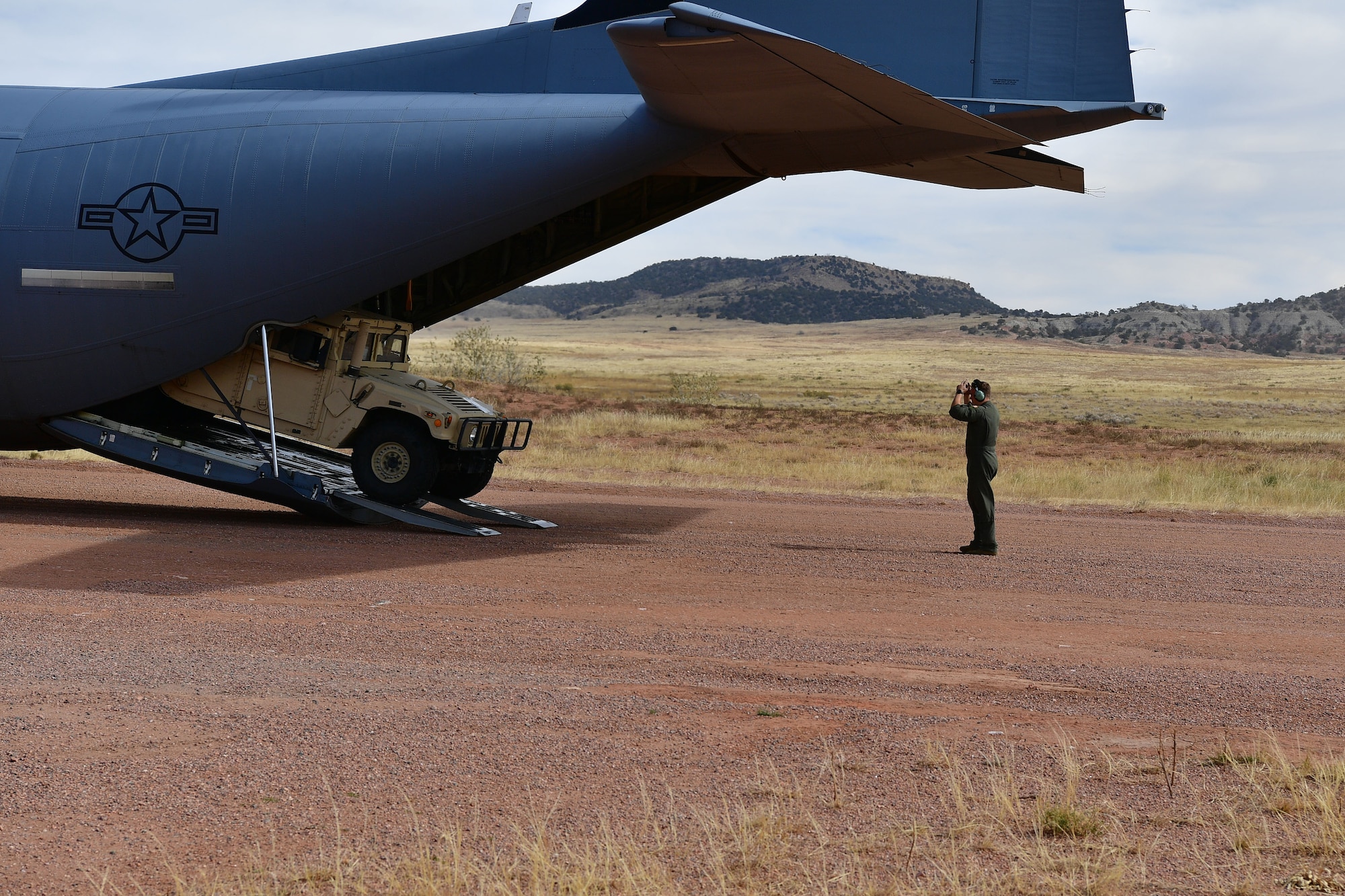 A loadmaster guides a humvee out the back of a C-130.