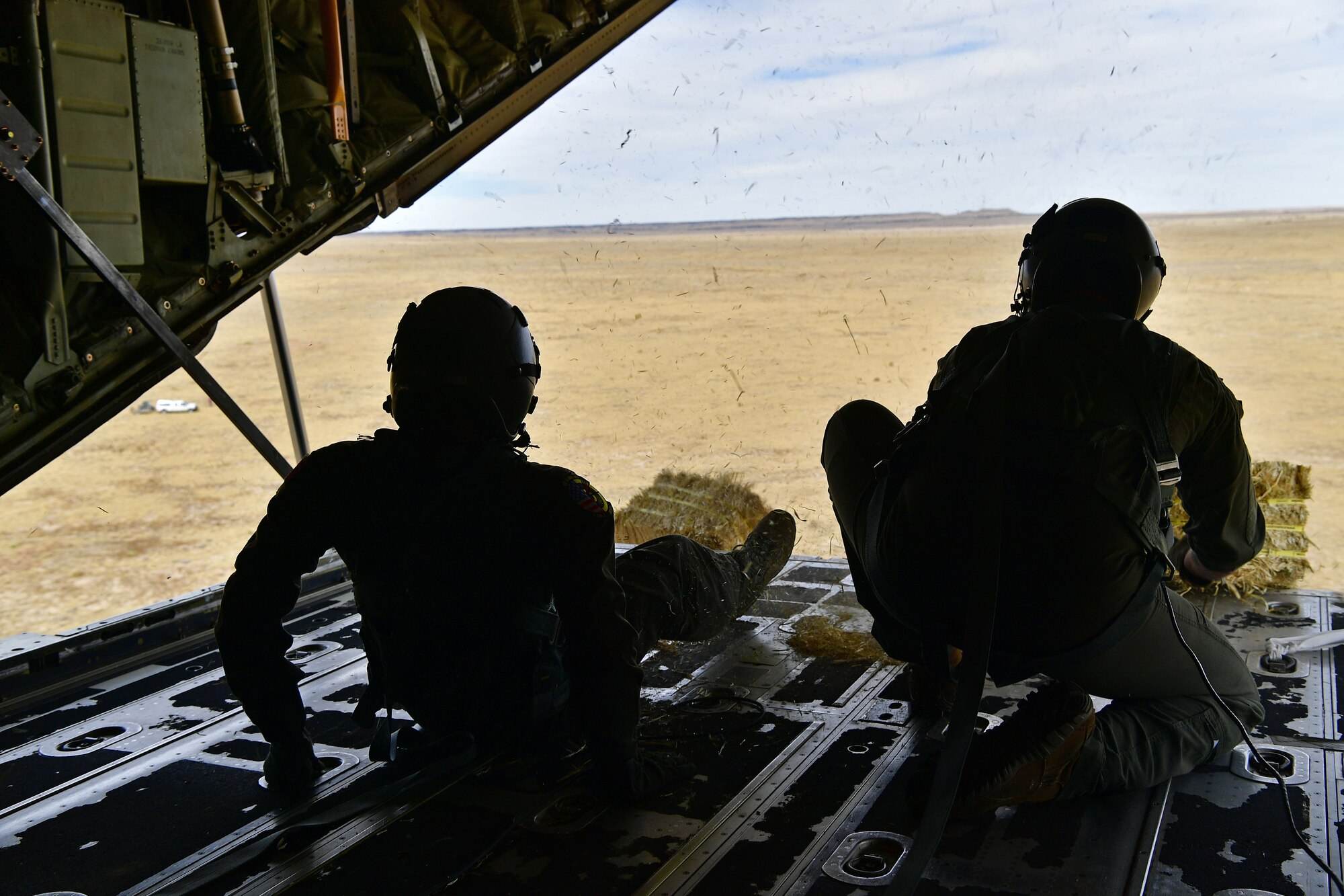 Loadmasters push a bundle out the back of a C-130.