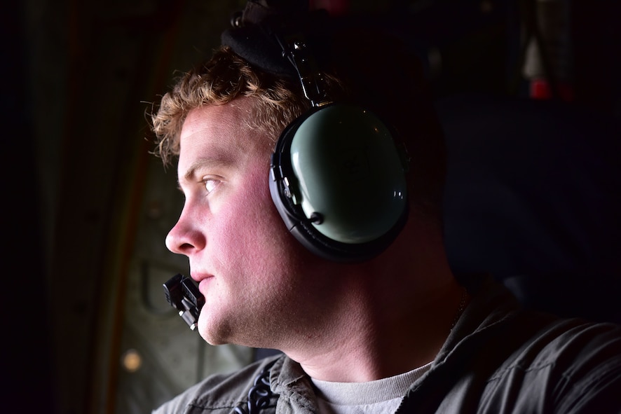 A loadmaster looks out the window of a C-130.