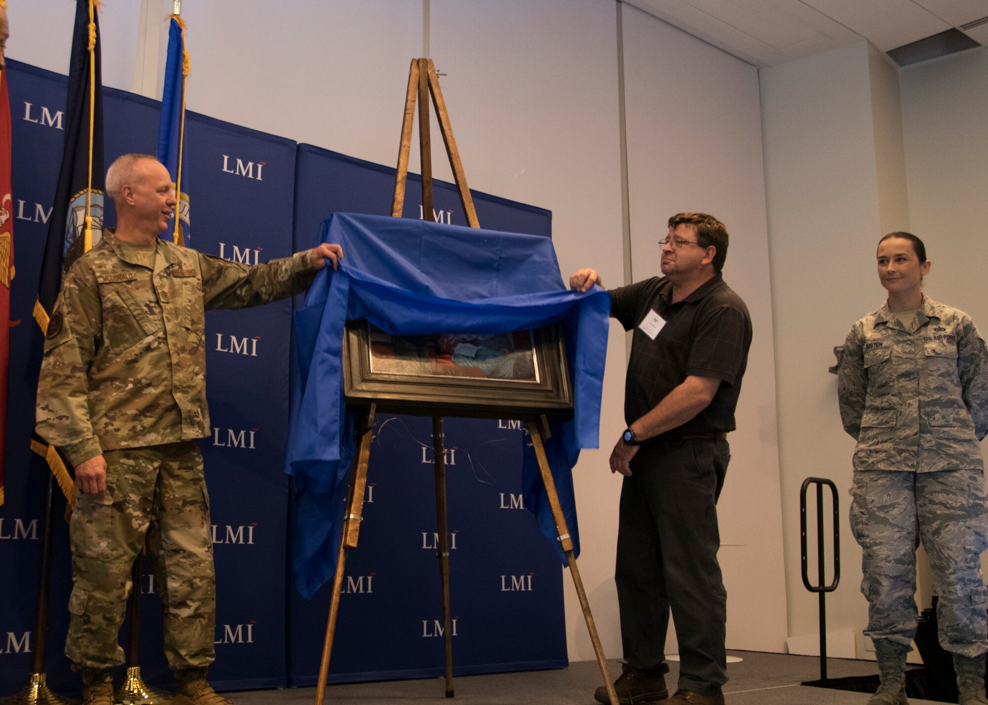 Tech Sgt. Kat Justen (right), Heritage and Combat Artist, Office of History and Heritage, Air Force Reserve Command, stands by during an art unveiling Sept. 19, 2019, at Logistics Management Institute in Tyson’s Corner, Va. Justen’s art portrayed Col. Clifford Zdanowicz, Jr., a dentist and 512th Aerospace Medicine Squadron Commander at Dover AFB and Navy HM1 Lisa-Marie Sasseville, Operational Health Support Unit, Dental Hygienist, providing dental services for a patient at the Burke County clinic site during the 2019 East Central Georgia Innovative Readiness Training Exercise. The joint exercise provided military members valuable hands-on experience and readiness training at five locations across five counties providing community members with no-cost medical services worth an estimated $1,355,000.
