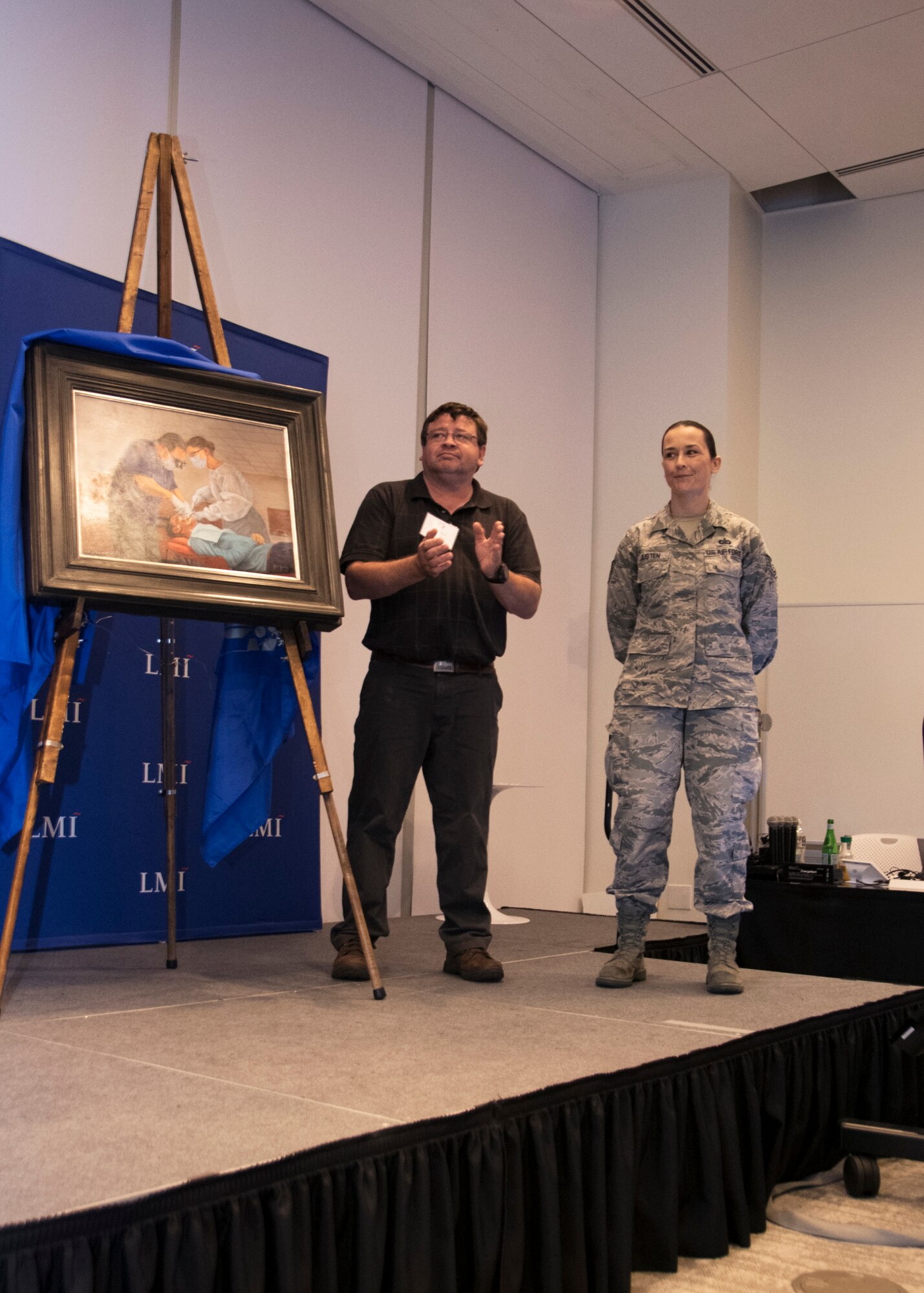 Tech Sgt. Kat Justen (right), Heritage and Combat Artist, Office of History and Heritage, Air Force Reserve Command, stands by during an art unveiling Sept. 19, 2019, at Tyson’s Corner, Va. Justen’s art portrayed Col. Clifford Zdanowicz, Jr., a dentist and 512th Aerospace Medicine Squadron Commander at Dover AFB