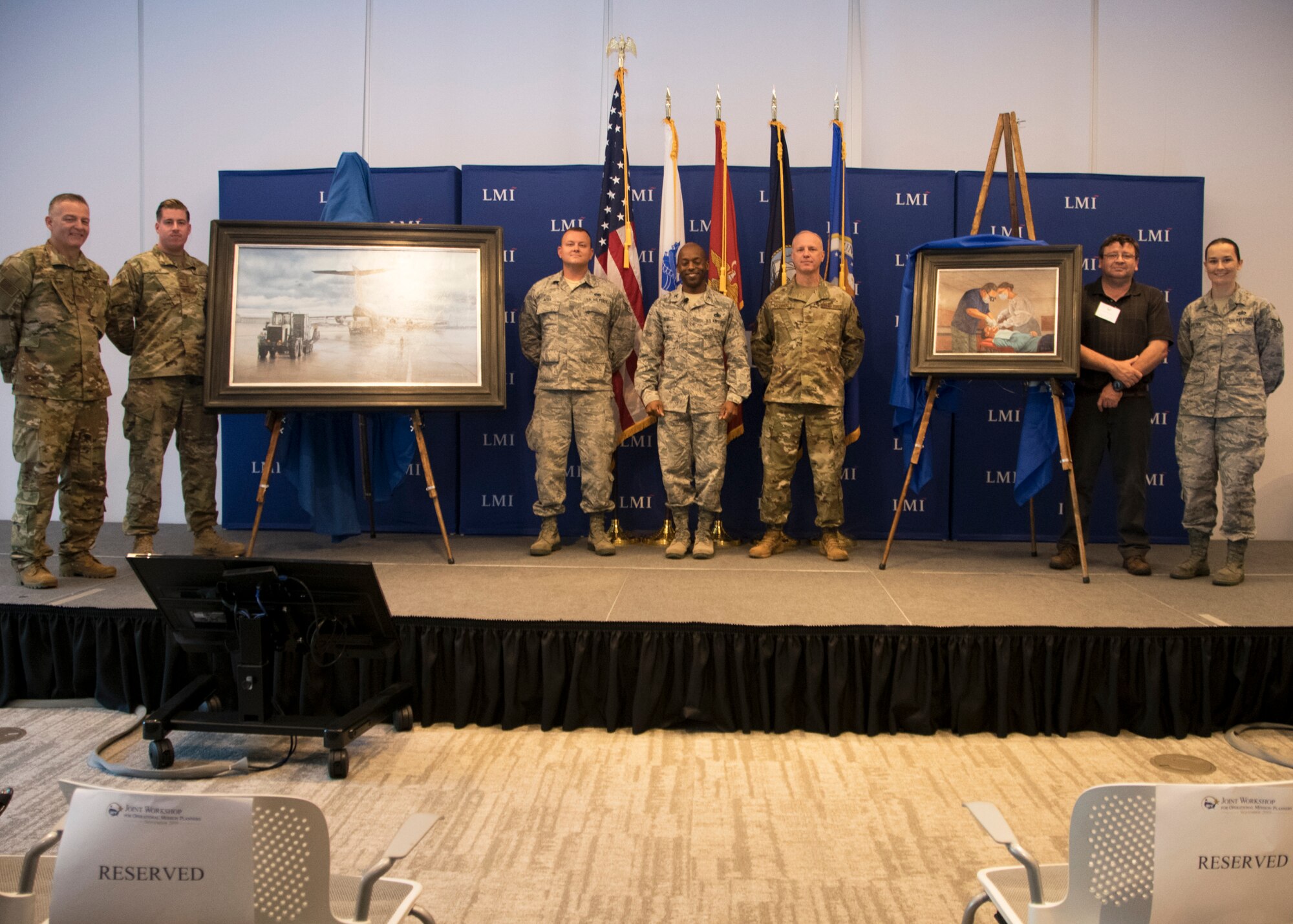 Tech Sgt. Kat Justen (far right) Heritage and Combat Artist, Office of History and Heritage, Air Force Reserve Command,  poses for a photo with participants in the Innovative Readiness Training Workshop after the “In their Care” painting unveiling Sept. 19, 2019, at the Logistics Management Institute in Tyson’s Corner, Va. Justen’s art portrayed Col. Clifford Zdanowicz, Jr., a dentist and 512th Aerospace Medicine Squadron Commander at Dover AFB and Navy HM1 Lisa-Marie Sasseville, Operational Health Support Unit, Dental Hygienist, providing dental services for a patient at the Burke County clinic site during the 2019 East Central Georgia Innovative Readiness Training Exercise. The joint exercise provided military members valuable hands-on experience and readiness training at five locations across five counties providing community members with no-cost medical services worth an estimated $1,355,000.