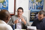 Three men pictured; man in center of picture is signing to another.