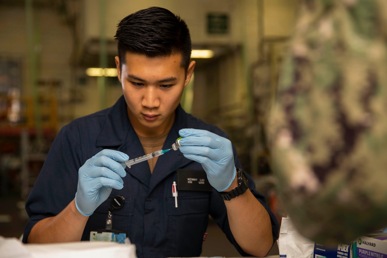 A sailor holds a syringe to a little bottle of liquid.