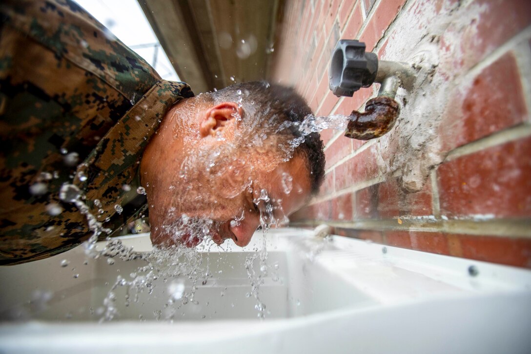 A Marine runs his face under a faucet at an outdoor sink