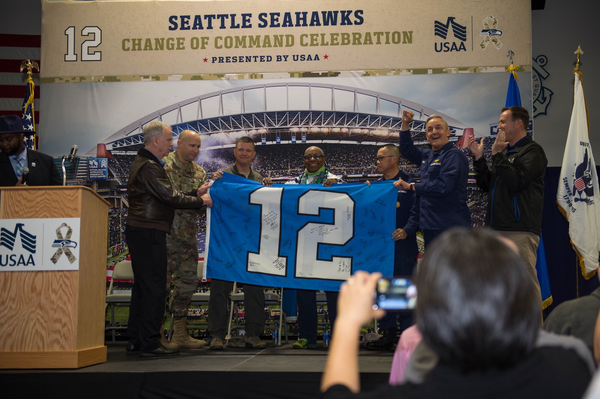 Members of the Seattle Seahawks organization, 62nd Airlift Wing and 13 Coast Guard District hold a 12th Man Flag during a “change of command” ceremony at Coast Guard Base Seattle, Wash., Oct. 22, 2019.