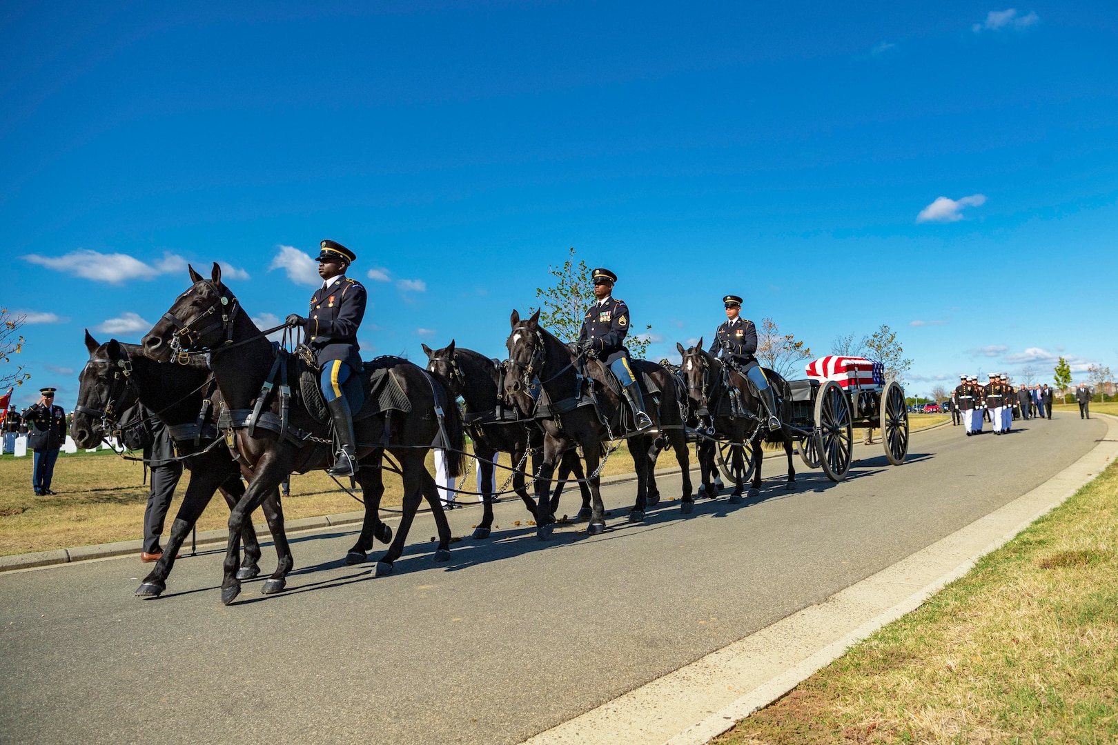 A group of soldiers ride horses escorting a coffin as Marines march behind.