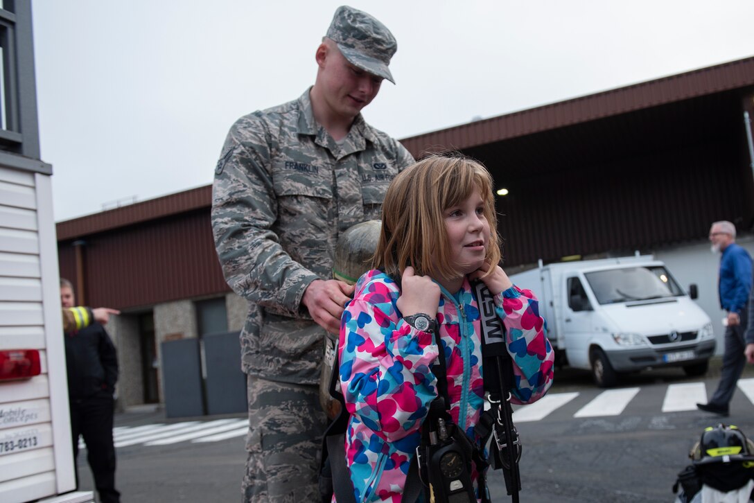 U.S. Air Force Airman 1st Class Brandon Franklin, 52nd Civil Engineer Squadron fire protection apprentice, helps a Spangdahlem Elementary School student try on an oxygen tank used by Spangdahlem firefighters at SPES on Spangdahlem Air Base, Germany, Oct. 23, 2019. For Fire Prevention Week, students were allowed to try on gear firefighters use when responding to fires. (U.S. Air Force photo by Airman 1st Class Alison Stewart)
