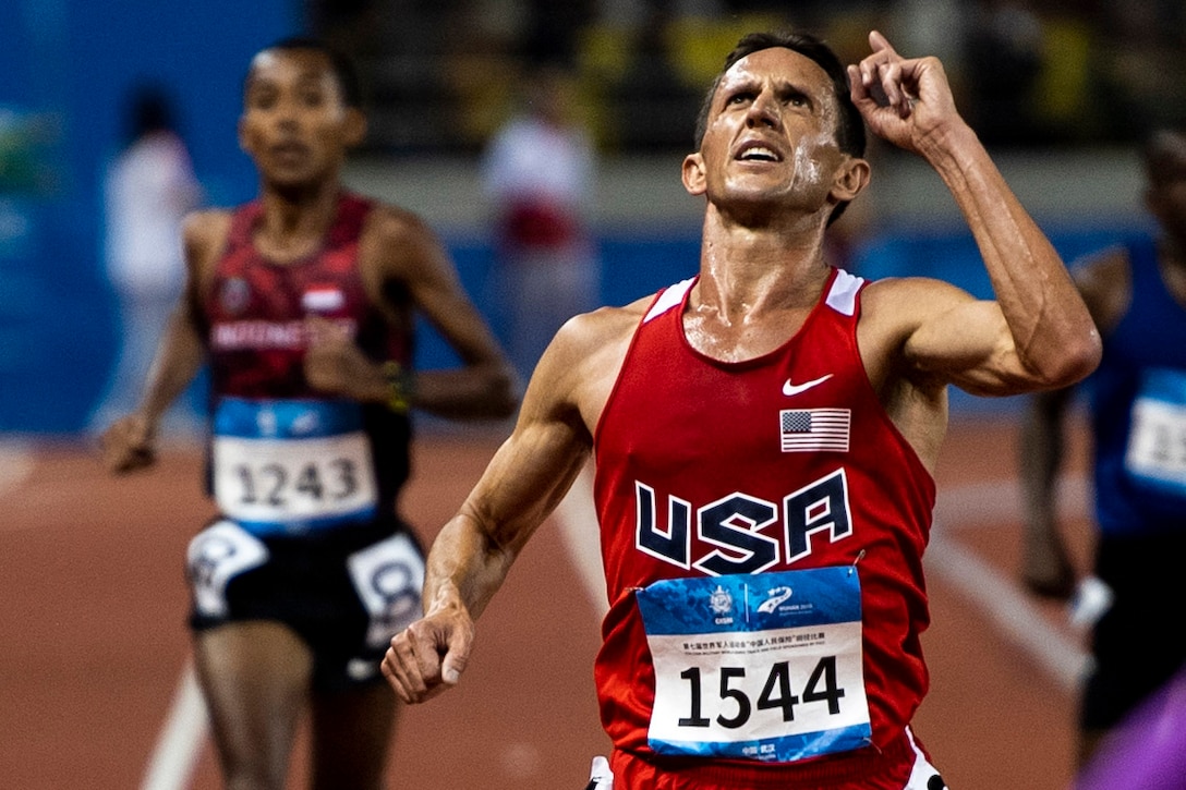 A military athlete points skywards as he finishes a track race.