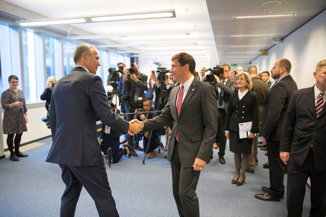 Two men shake hands in front of a large number of reporters.