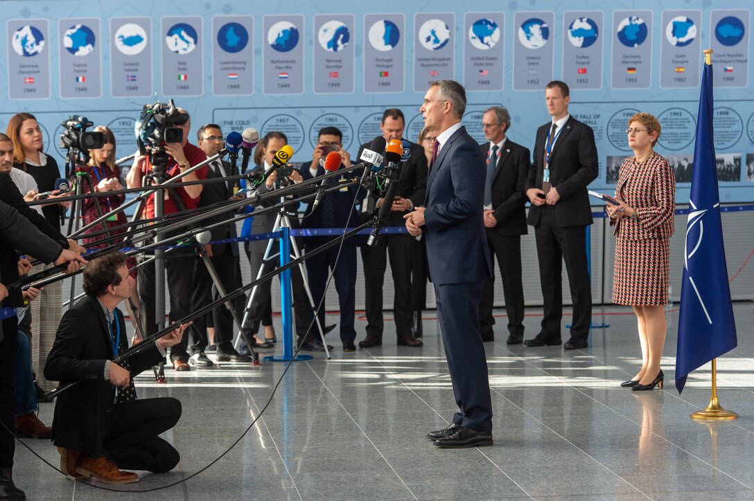 Man surrounded by reporters delivers remarks.