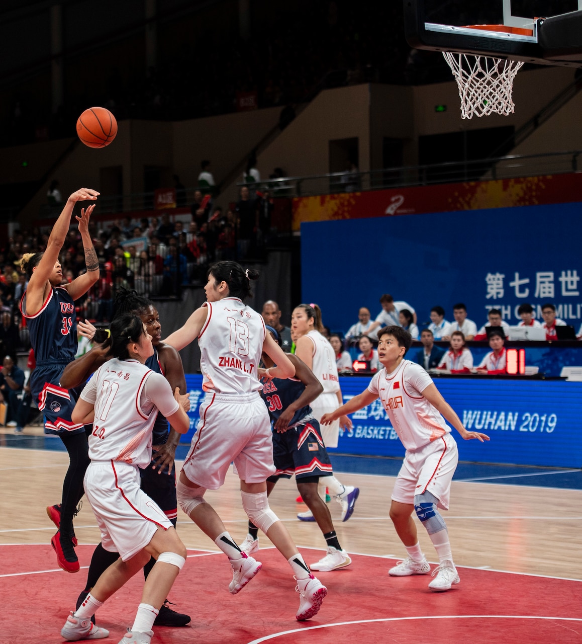 Basketball player launches a jump shot amid four defenders.