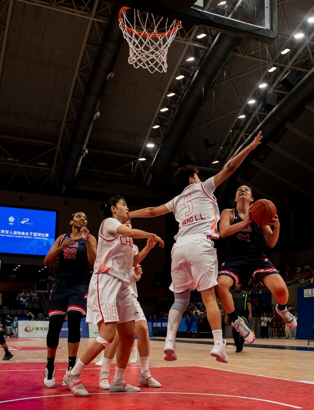 Basketball player holding the ball jumps to make a shot, closely guarded by a defender.