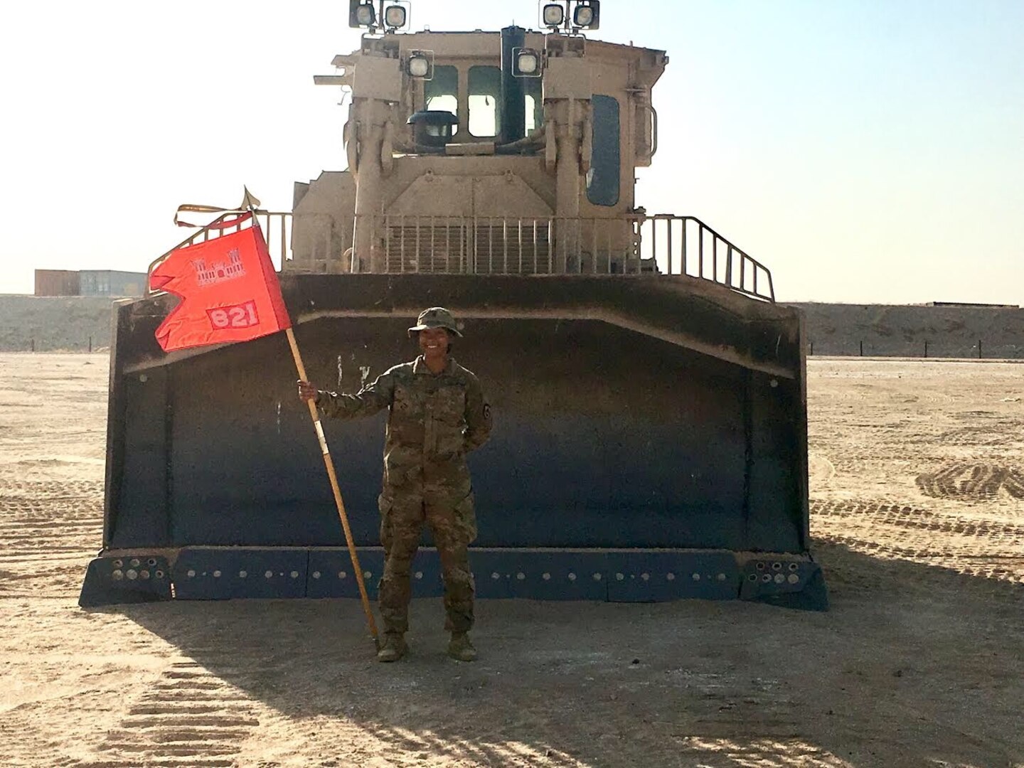 Spc. Amia Adkins stand in front of a bulldozer in the Middle East, holding the WVNG's 821st Engineer Company Gideon.