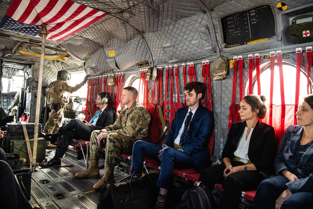 People sit aboard an airborne helicopter with the door open.