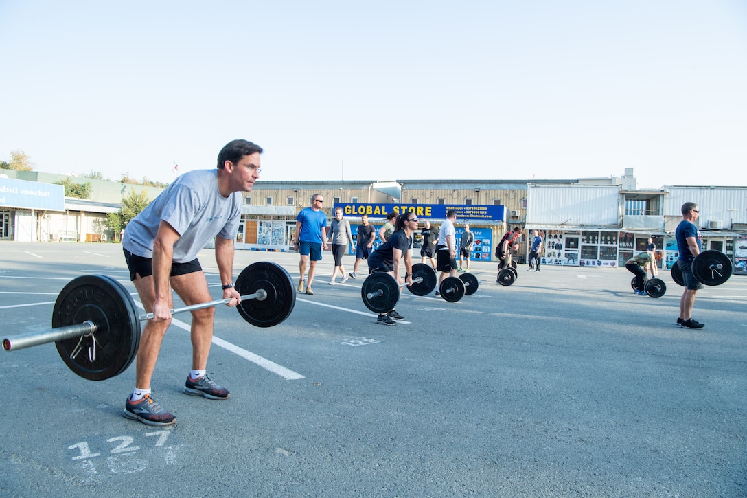 Defense secretary lifts weights with several other people.