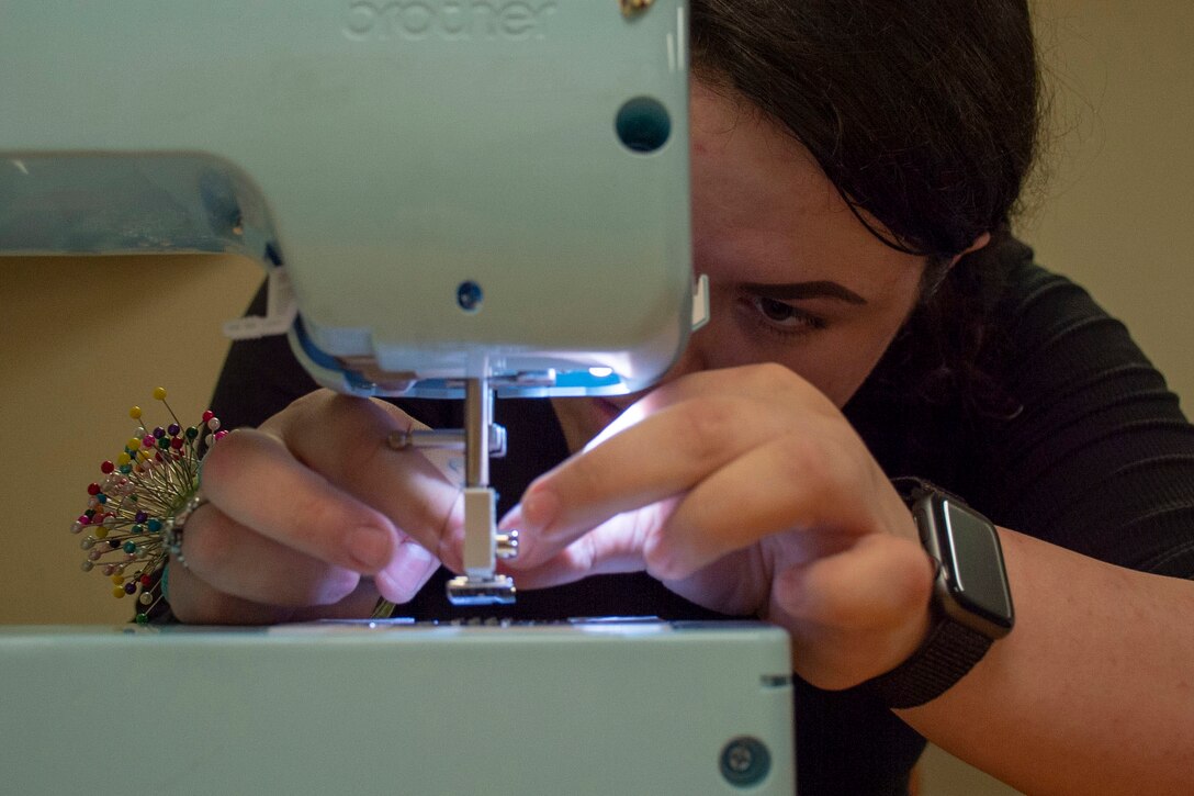 A woman looks closely as she threads a needle under a small light.