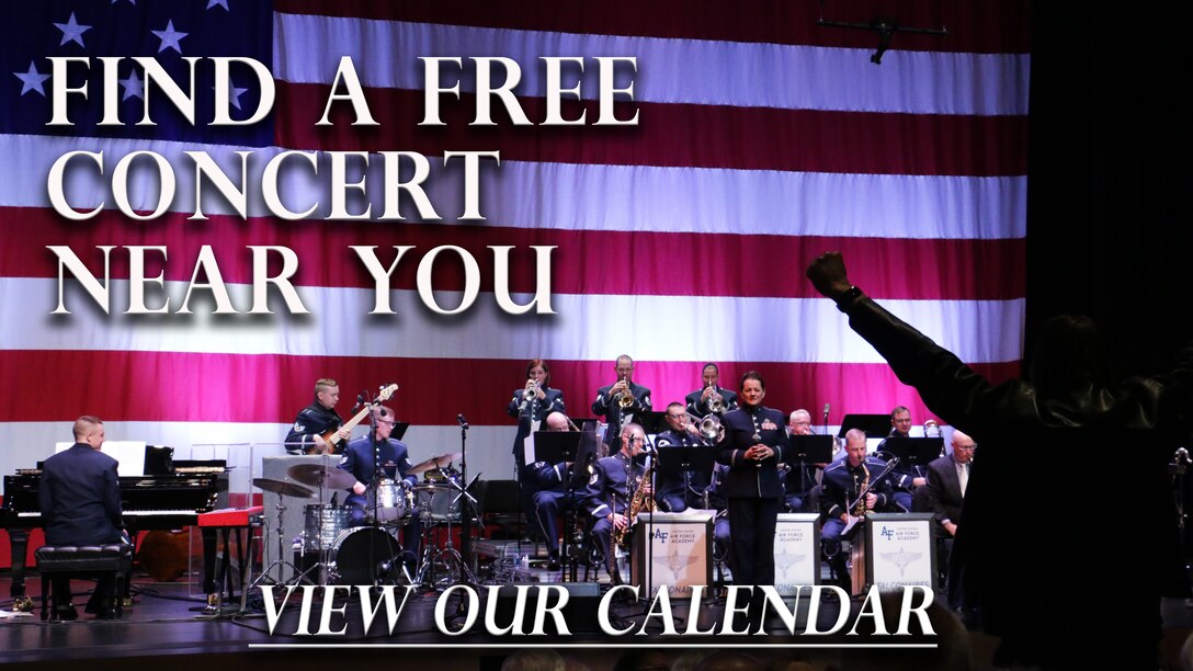 The Falconaires jazz band performs in front of a huge American flag in their blue tunic uniforms as a veteran in the audience stands to be recognized for his service and raises his arms over his head in a proud V.