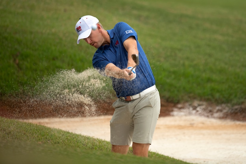 Sand sprays as a golfer hits out of a bunker.