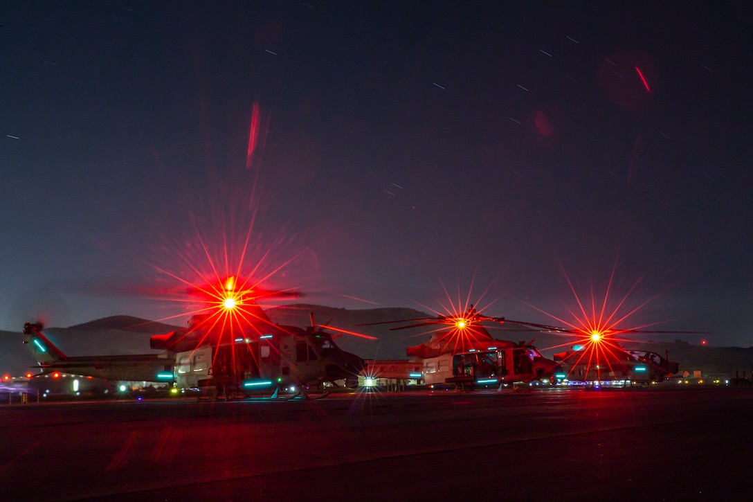 Three helicopters with red lights sit on the tarmac at night.