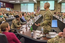 man in army uniform speaks to a crowd of people.