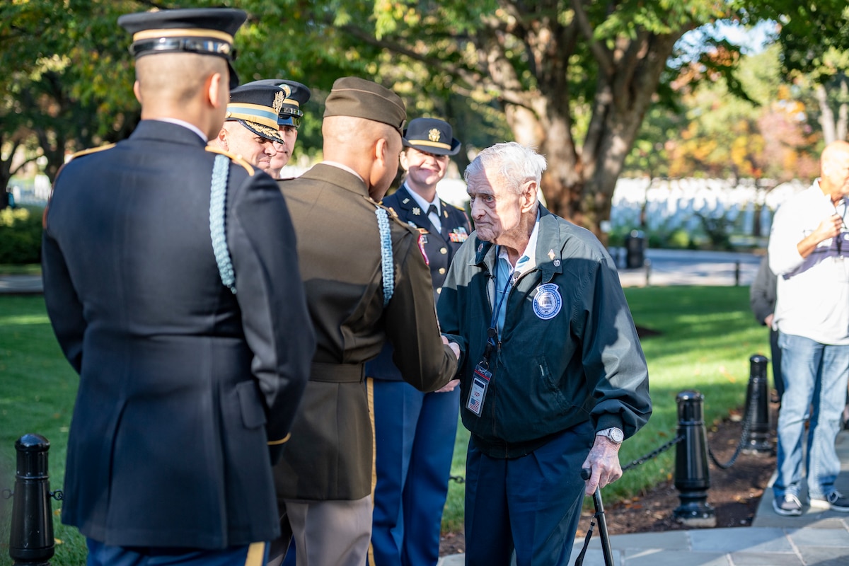 A veteran exchanges greetings with service members at a cemetery.