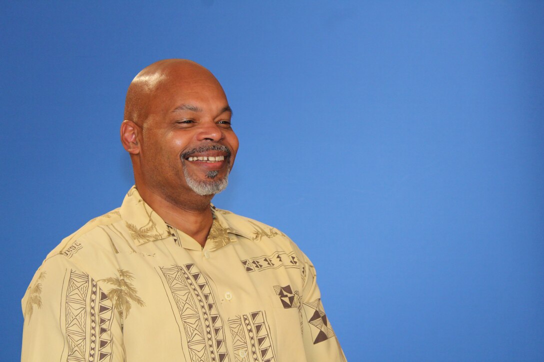 G Galloway (known as “G”) Director of Cybersecurity at NSA Hawai’i sits in front of a Blue screen.