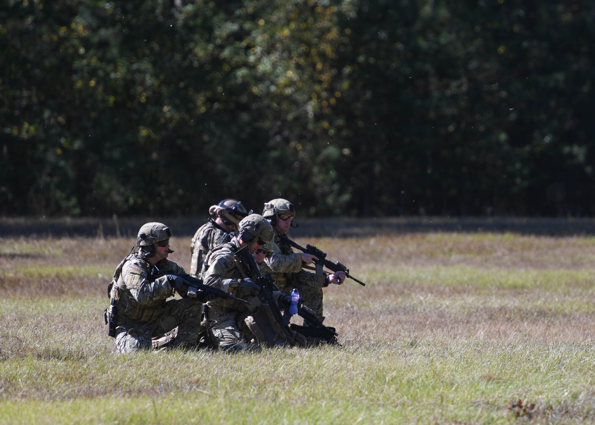 Airman kneel on a grass field holding M4's