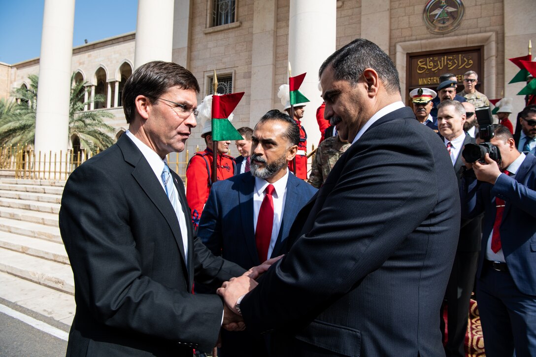 Two men shake hands as a third man looks on outside government building.