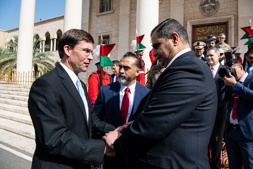 Two men shake hands as a third man looks on outside government building.