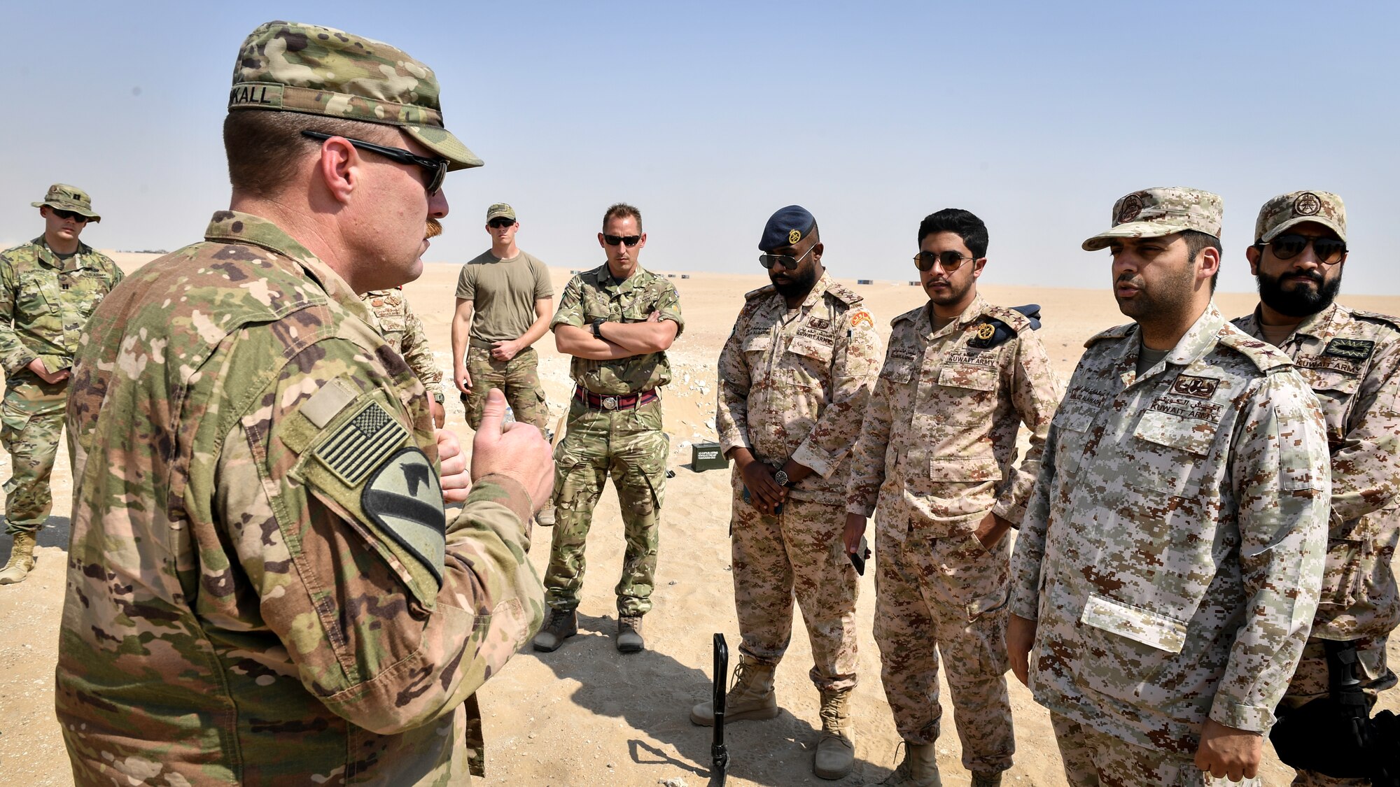 U.S. Army 1st Sgt. Adam Blunkall, 744th Ordnance Company first sergeant, speaks with Kuwaiti Ministry of Defense EOD technicians before an insensitive munitions disposal training at the Udari Range, Kuwait, Sept. 30, 2019. The training was designed for U.S. and Kuwaiti forces to share techniques, synchronize capabilities and build partnerships.