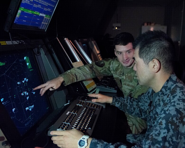 Staff Sgt. Brian Ludjack, 374th Operations Support Squadron air traffic watch supervisor, explains to Koku-Jieitai Tech. Sgt. Kenji Nariyama, 2nd mobile Squadron aircraft control and warning technician assigned with Iruma Air Base, Japan, how they monitor and control aircraft in the radar approach control section of the air traffic control tower, Oct. 23, 2019, at Yokota Air Base.