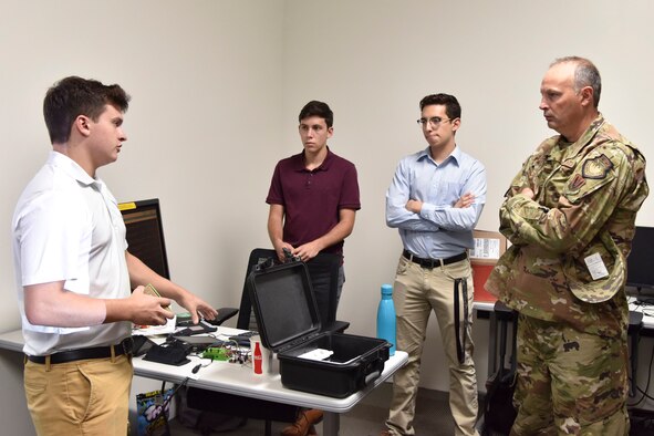 Matthew Santalla, a senior at Florida Polytechnic University majoring in Business Analytics and Quantitative Economics, briefs Col. Chad Hartman, commander of the Air Force Technical Applications Center, on a system he and four other university students developed during their X-Force summer fellowship with the nuclear treaty monitoring center at Cape Canaveral Air Force Station, Fla.  The program is sponsored by the National Security Innovation Network.  Pictured left to right:  Santalla; Andrew Bass, a freshman at Washington University in St. Louis;  Bryan Urias, a senior at Florida Polytechnic University; and Hartman. (U.S. Air Force photo by Matthew S. Jurgens)