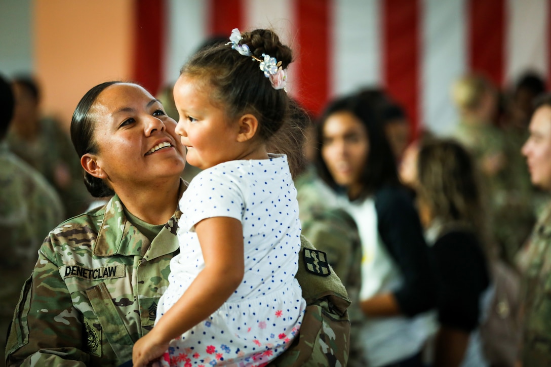 A soldier holds her daughter in her arms.