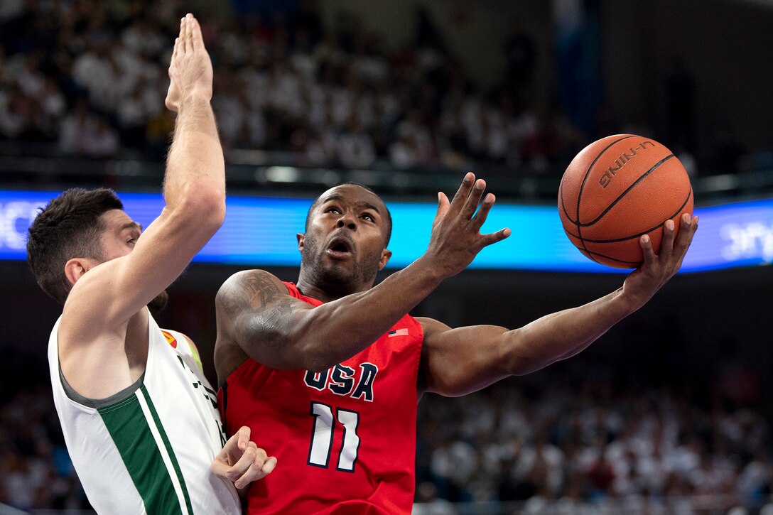 A Marine Corps athlete jumps with a basketball as a player on the other team tries to block.