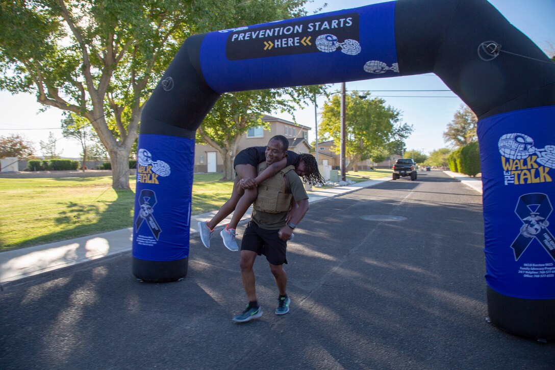 Major Ernest Robinson, Operations officer, finishes the Domestic Violence Awareness Run/Walk strong, carrying his 9-year-old daughter Maegon across the finish line aboard Marine Corps Logistics Base Barstow, Calif., Oct. 23. The event raises awareness of and support for victims and survivors of domestic violence in a fun, healthy, family-friendly manner.