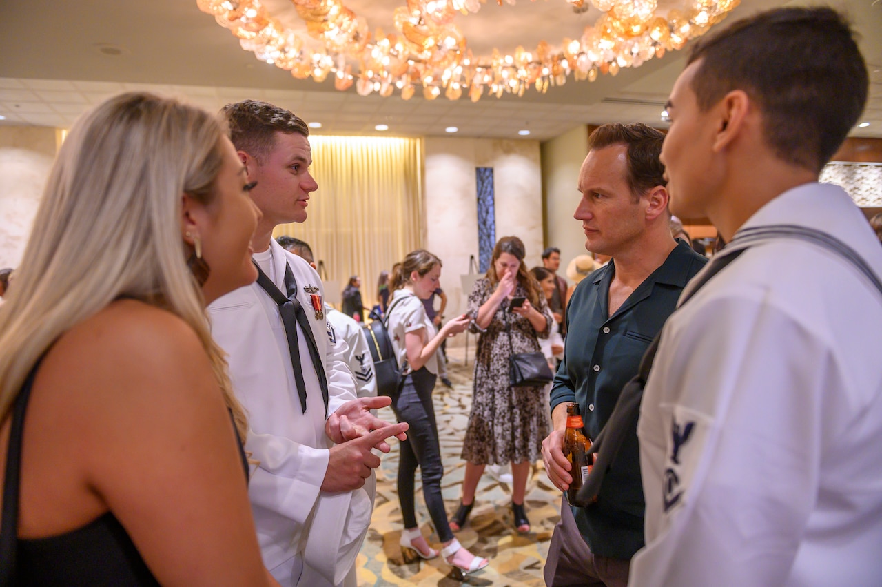 Two sailors in dress uniform and a woman in a dress speak with actor Patrick Wilson while standing in a circle at a gala.