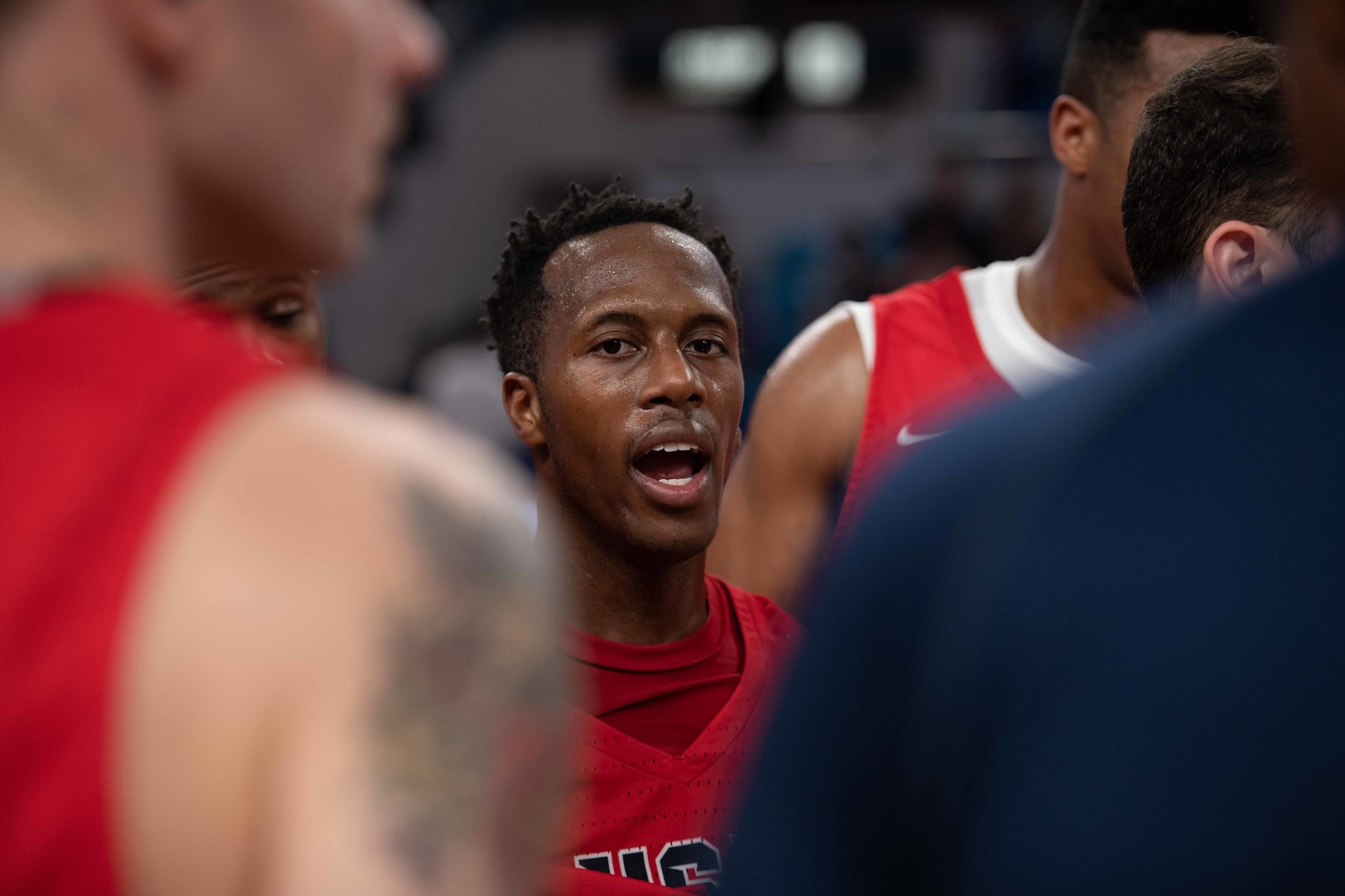 Basketball player framed by teammates in soft focus shouts encouragement.