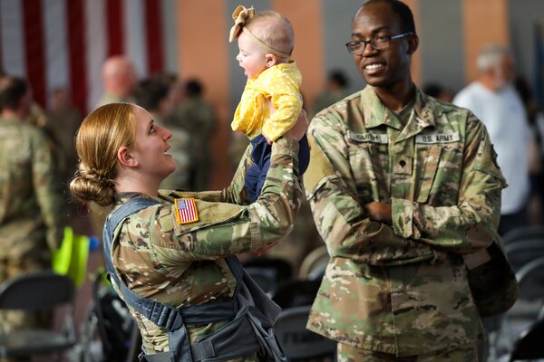 A soldier holds her baby as another soldier looks on.