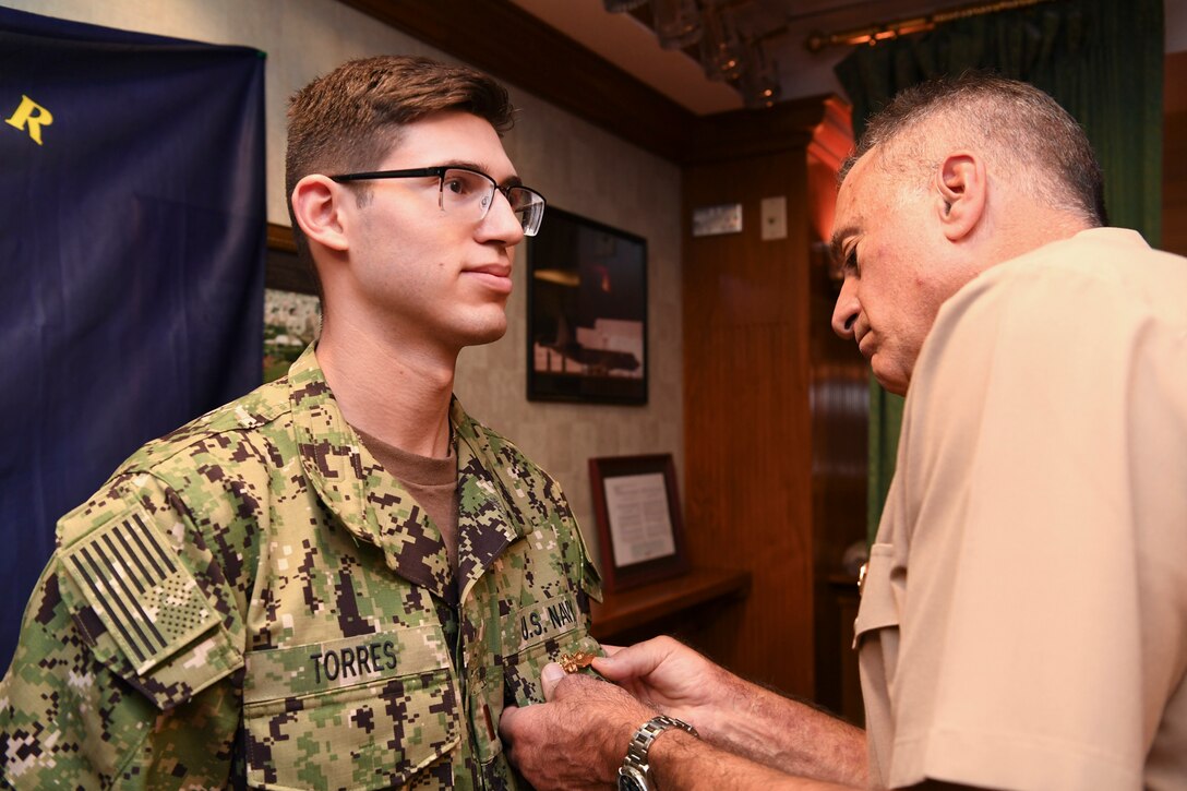 191023-N-KZ419-1040 NAVAL SUPPORT ACTIVITY BAHRAIN, Bahrain (Oct. 23, 2019) Rear Adm. Jack Buono, Superintendent of the U.S. Merchant Marine Academy, pins Ensign Ryan Torres with his Strategic Sealift Officer Warfare Insignia during after a tour of the Naval Coordination and Guidance for Shipping (NCAGS) facilities. The U.S. Naval Forces Central Command (NAVCENT) NCAGS team has recently amplified their support to the region in support of Operation Sentinel, a multinational maritime security effort designed to increase surveillance of key waterways in the Middle East to ensure freedom of navigation. (U.S. Navy photo by Mass Communication Specialist 3rd Class Dawson Roth/Released)