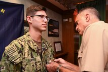 191023-N-KZ419-1040 NAVAL SUPPORT ACTIVITY BAHRAIN, Bahrain (Oct. 23, 2019) Rear Adm. Jack Buono, Superintendent of the U.S. Merchant Marine Academy, pins Ensign Ryan Torres with his Strategic Sealift Officer Warfare Insignia during after a tour of the Naval Coordination and Guidance for Shipping (NCAGS) facilities. The U.S. Naval Forces Central Command (NAVCENT) NCAGS team has recently amplified their support to the region in support of Operation Sentinel, a multinational maritime security effort designed to increase surveillance of key waterways in the Middle East to ensure freedom of navigation. (U.S. Navy photo by Mass Communication Specialist 3rd Class Dawson Roth/Released)