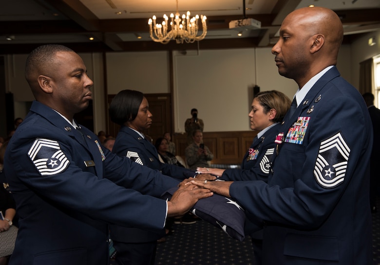 Retired U.S. Air Force Chief Master Sgt. Robinson Joseph, right, former U.S. Air Forces in Europe – Air Forces Africa Chief Enlisted Manager for the Air Force Installation Contracting Center, and his wife, retired Chief Master Sgt. Leenette Joseph, former USAFE Equal Opportunity functional manager, receive U.S. flags at their retirement ceremony on Ramstein Air Base, Germany, Oct. 25, 2019. During their careers, the Josephs served a combined 52 years, 21 assignments and 8 deployments.