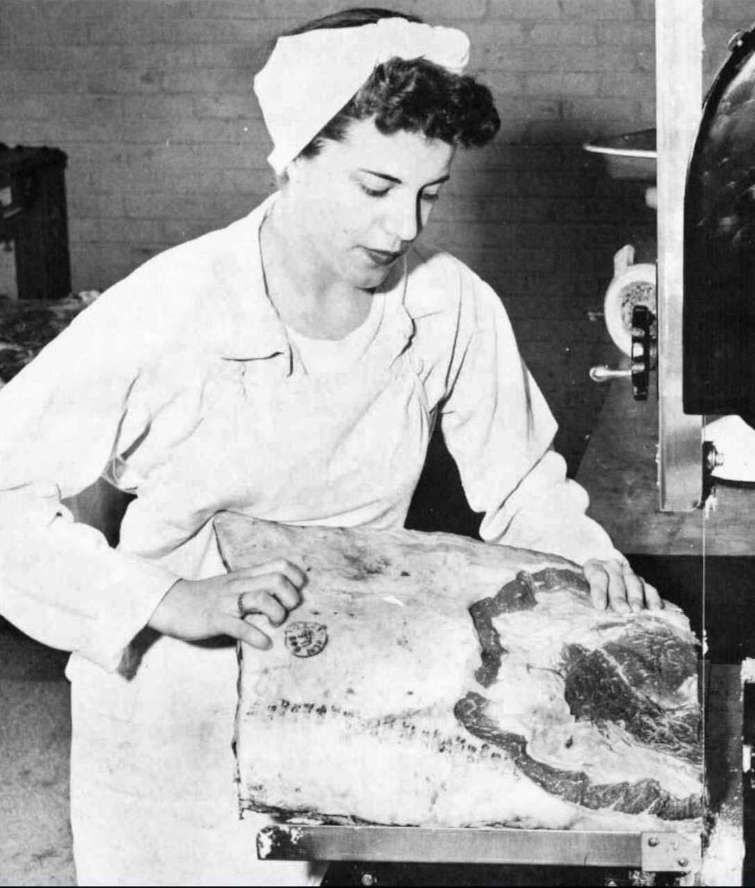 A woman cuts meat with a bandsaw.