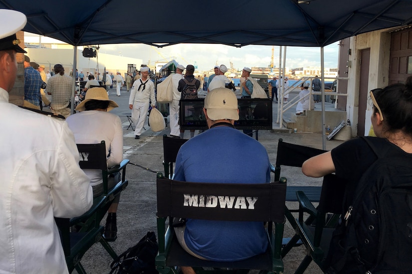 A group of people sit in chairs watching  the filming of a movie.