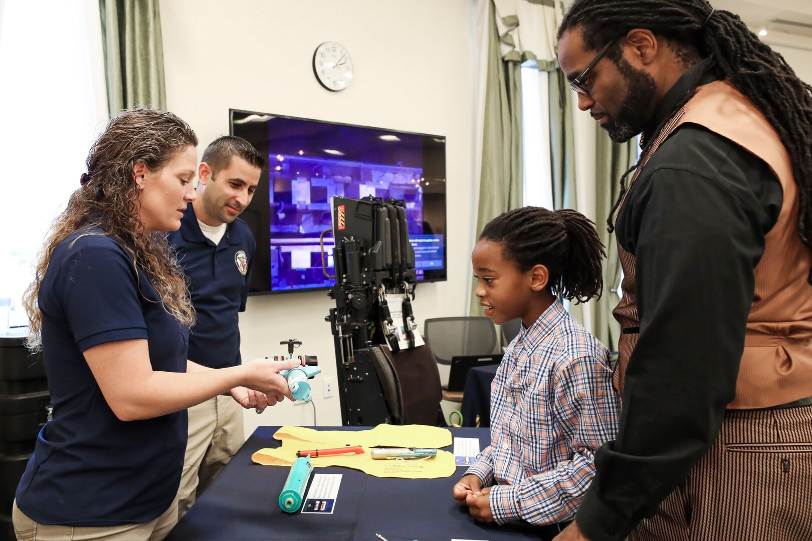 NSWC IHEODTD Acquisition Management Specialist Jessica Schombs and NSWC IHEODTD Equipment Specialist Nick Schombs of the CAD/PAD Division explain the components of an ejection seat to Antwan Proctor and his eight-year-old son Antwan Proctor, Jr. at the STEM Fest event held at Waldorf West Public Library, Oct. 26.
