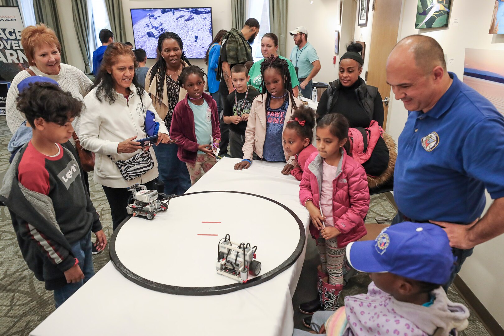 NSWC IHEODTD engineer John Kilikewich of the CAD/PAD Division looks on as students and parents watch Lego robots autonomously sumo wrestle at the STEM Fest event held at Waldorf West Public Library, Oct. 26 .  (U.S. Navy photo by Matthew Poynor)