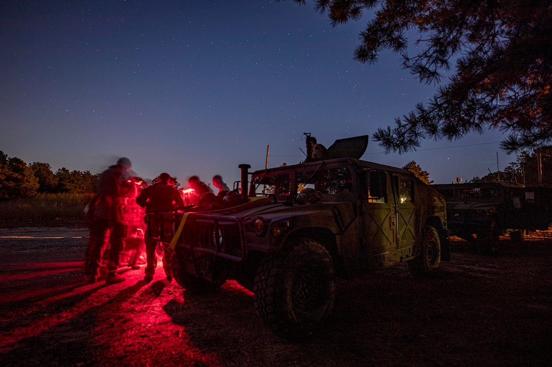 Airmen, illuminated in red light, gather by a military vehicle at night.