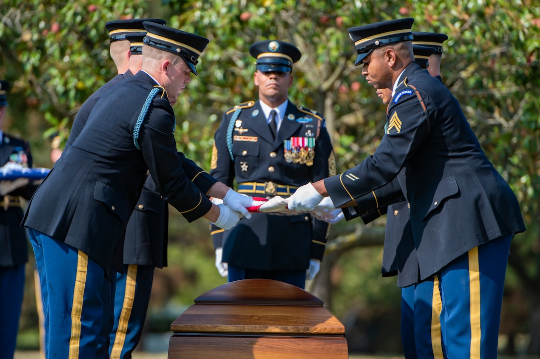 Soldiers fold a flag over a wooden casket.